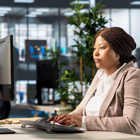 Woman working at a computer in an office with pants behind her.