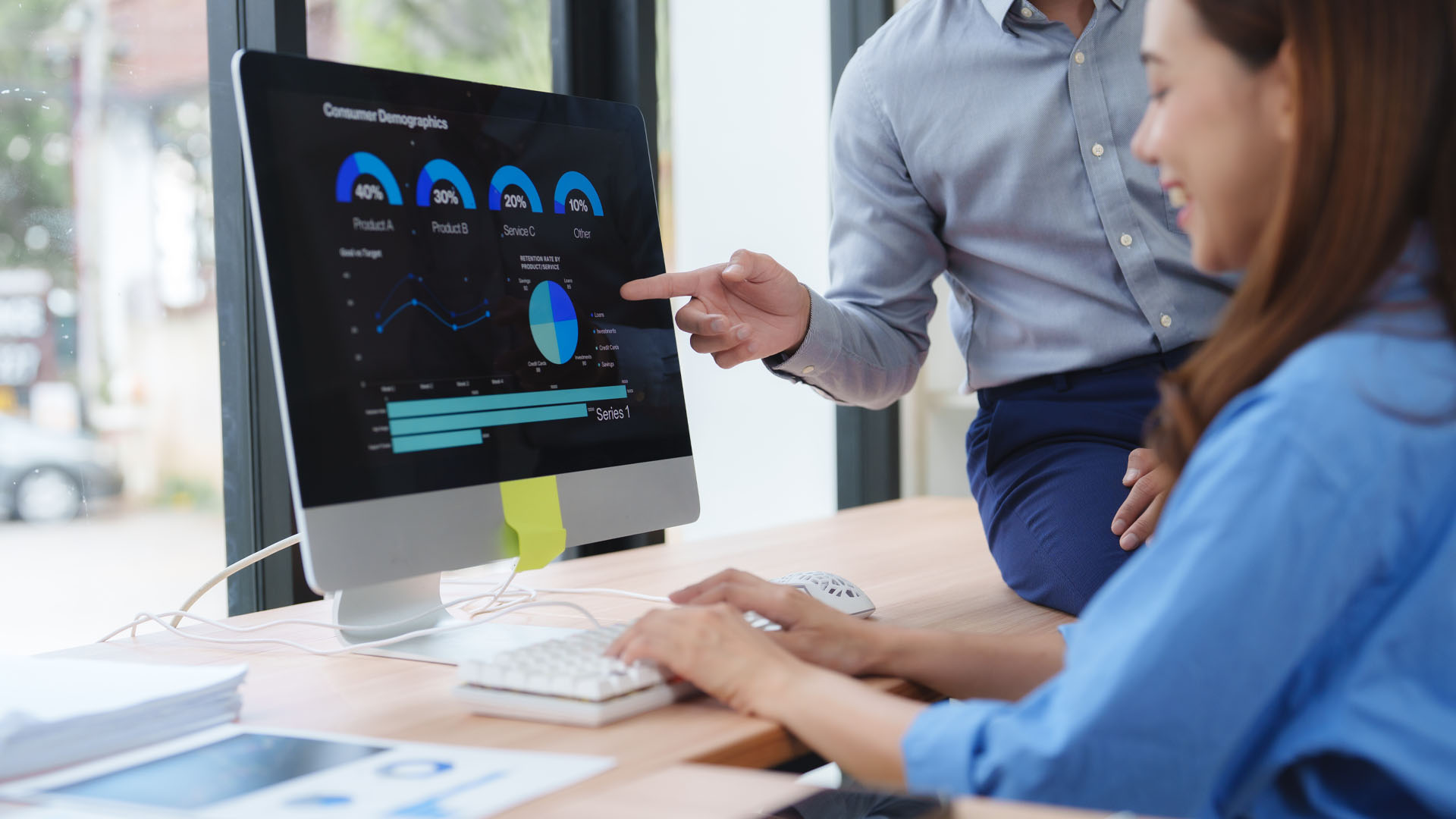 Two coworkers reviewing data charts on a desktop screen in an office.
