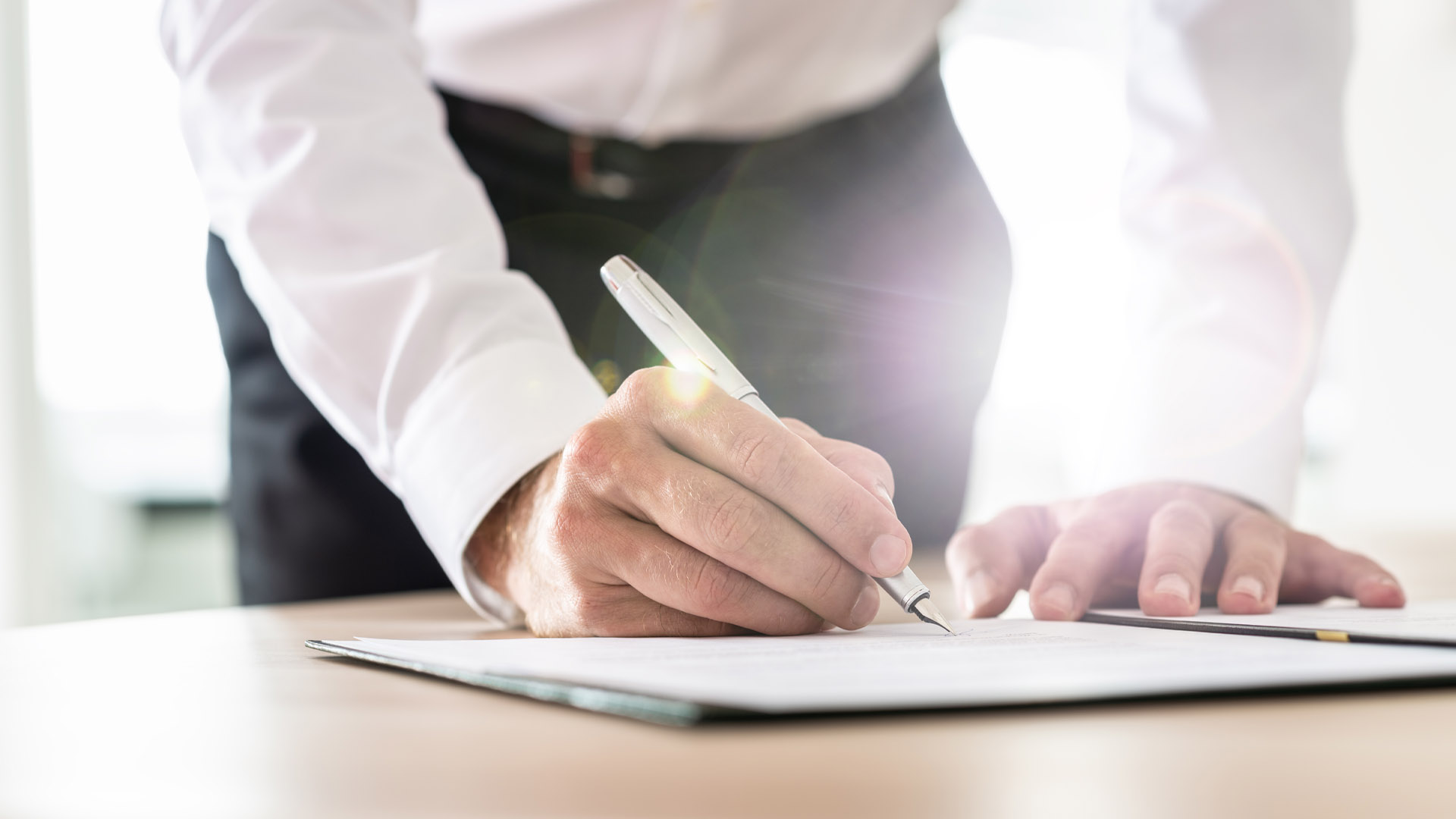 Close-up of a person signing a document with a pen on a desk.