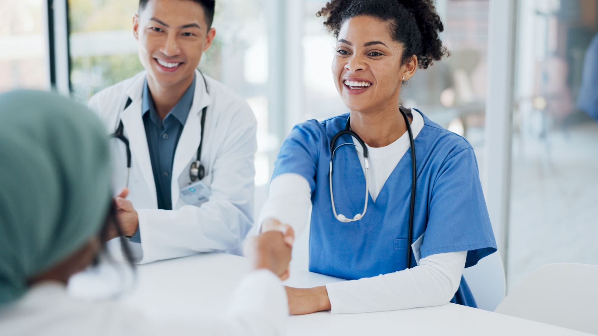 Two healthcare professionals smiling and shaking hands with a patient.