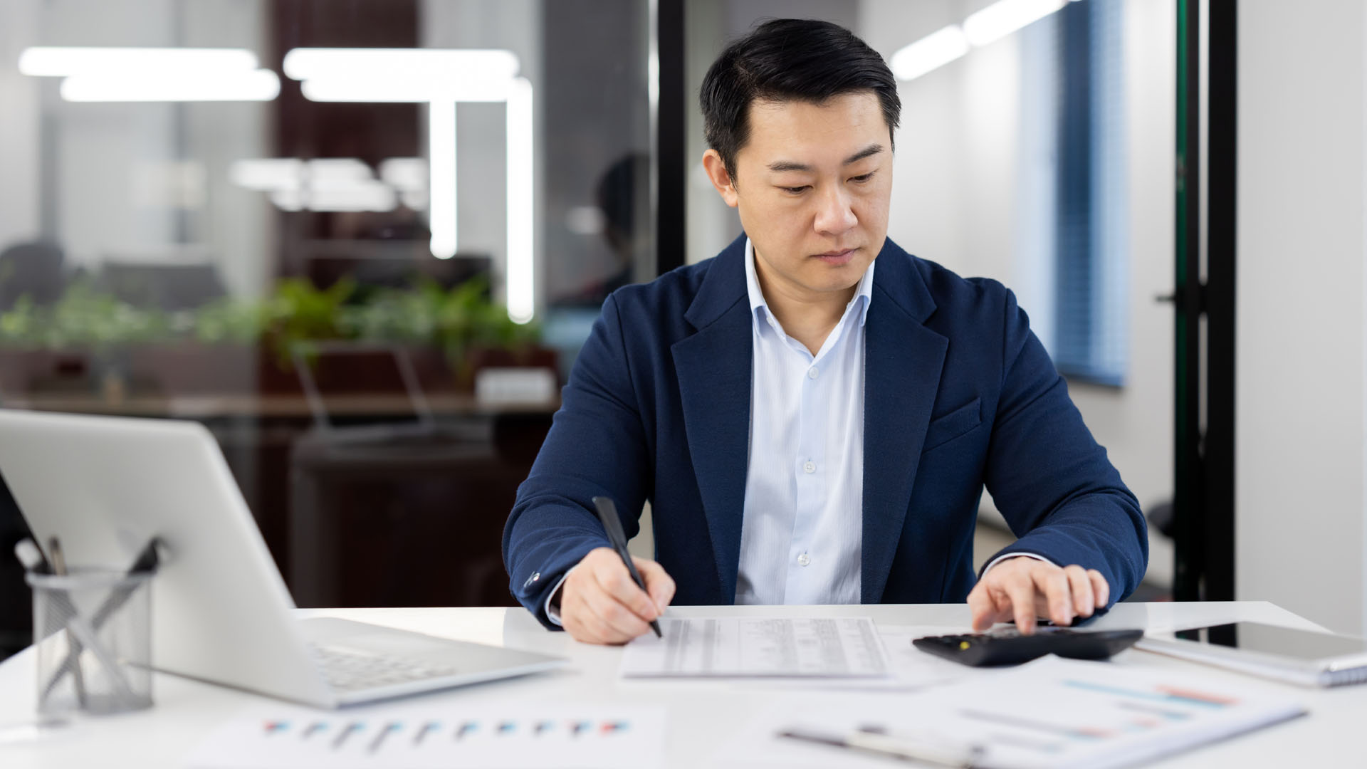 Man reviewing paperwork and using a calculator at a desk.